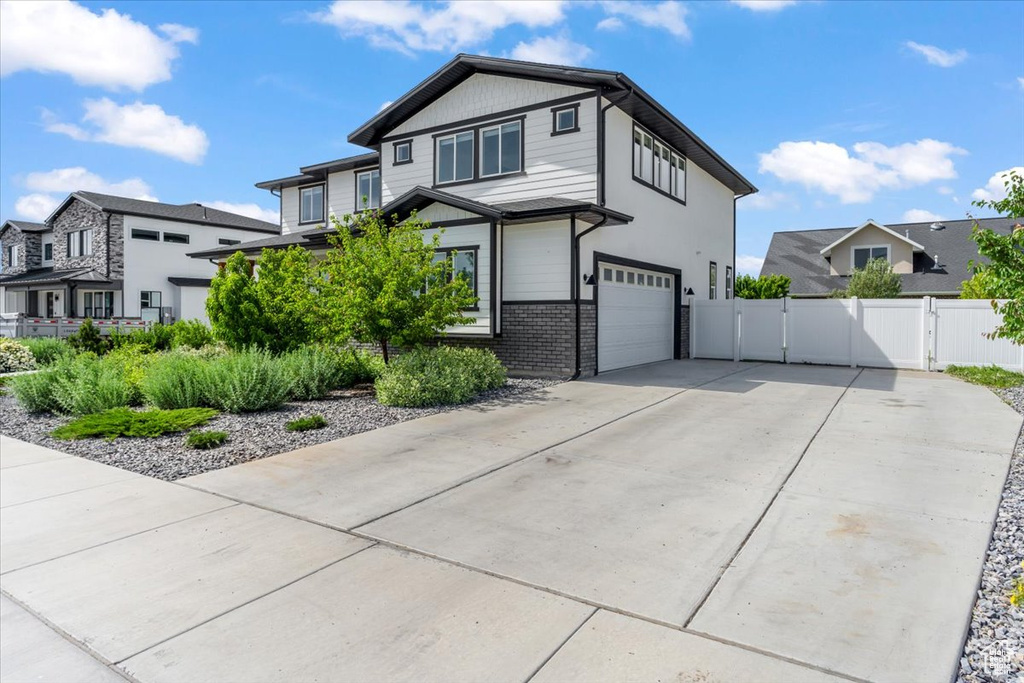 View of front of home with a gate, a garage, driveway, a residential view, and brick siding