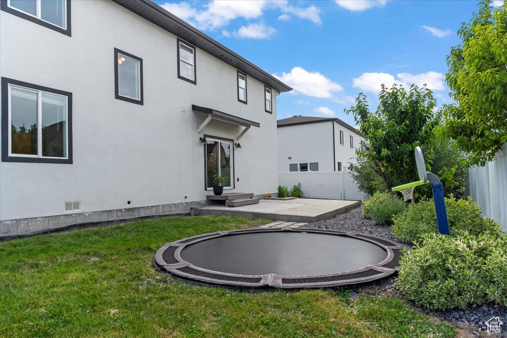 Back of house with a trampoline, stucco siding, and a patio area