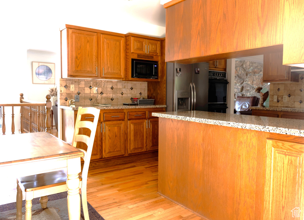 Kitchen with black appliances, decorative backsplash, brown cabinetry, and light wood-style flooring