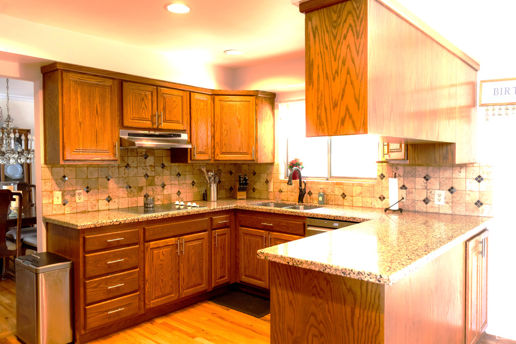 Kitchen with a sink, under cabinet range hood, black electric stovetop, a peninsula, and brown cabinets