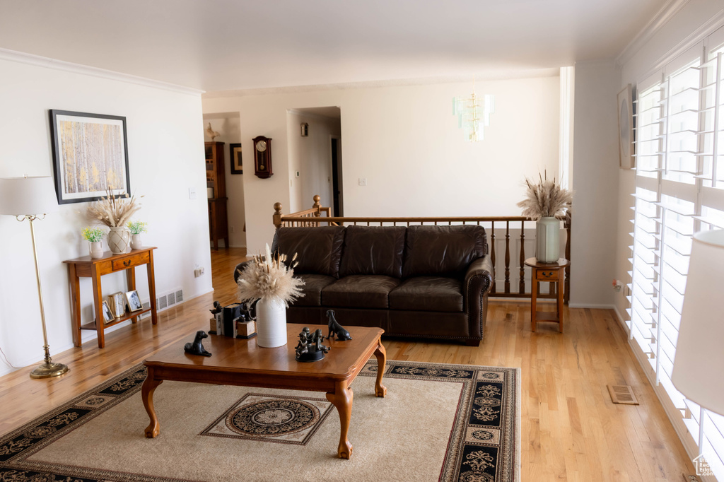 Living area with light wood finished floors, plenty of natural light, crown molding, and a chandelier