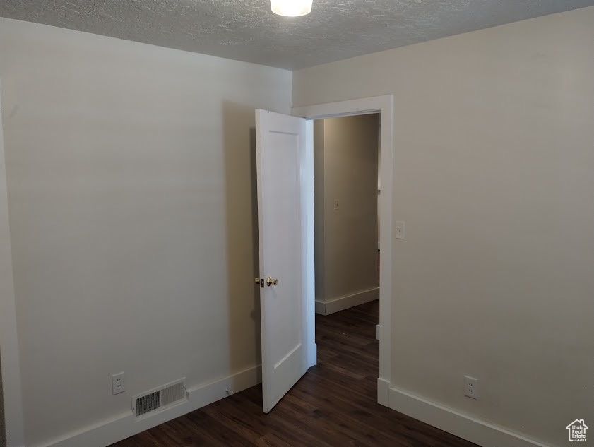 Spare room with baseboards, dark wood-type flooring, and a textured ceiling