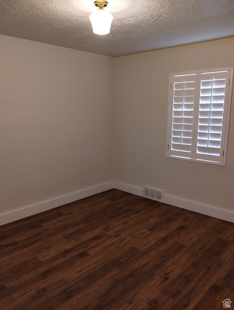 Spare room with dark wood-type flooring, a textured ceiling, and baseboards