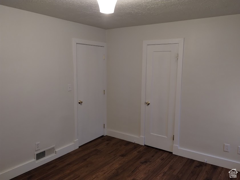 Empty room featuring dark wood-style floors, a textured ceiling, and baseboards