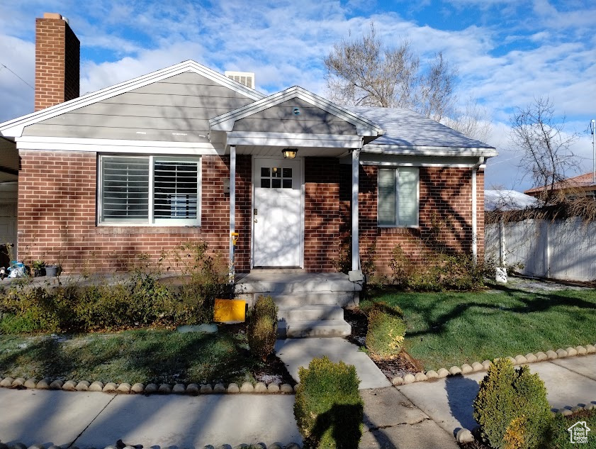 View of front facade featuring brick siding, a chimney, and a front lawn