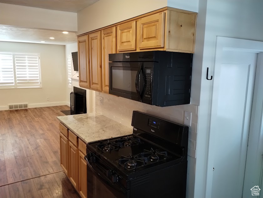 Kitchen with black appliances, wood finished floors, baseboards, light stone counters, and light brown cabinets