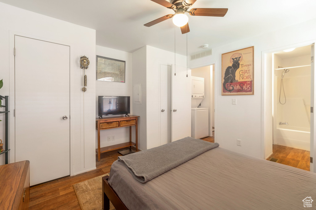 Bedroom with estacked washer and dryer, wood finished floors, ensuite bath, and a ceiling fan