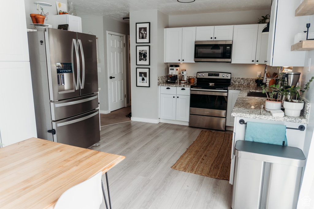 Kitchen featuring appliances with stainless steel finishes, open shelves, white cabinets, light wood-style flooring, and light stone counters