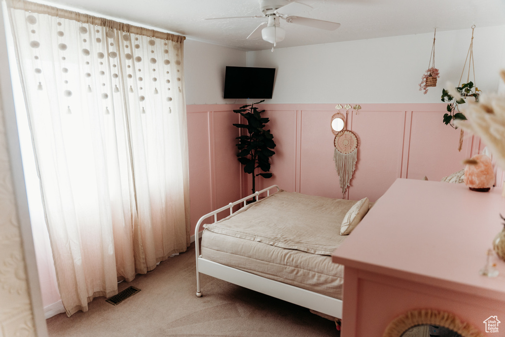 Bedroom with light carpet, a decorative wall, a wainscoted wall, and ceiling fan