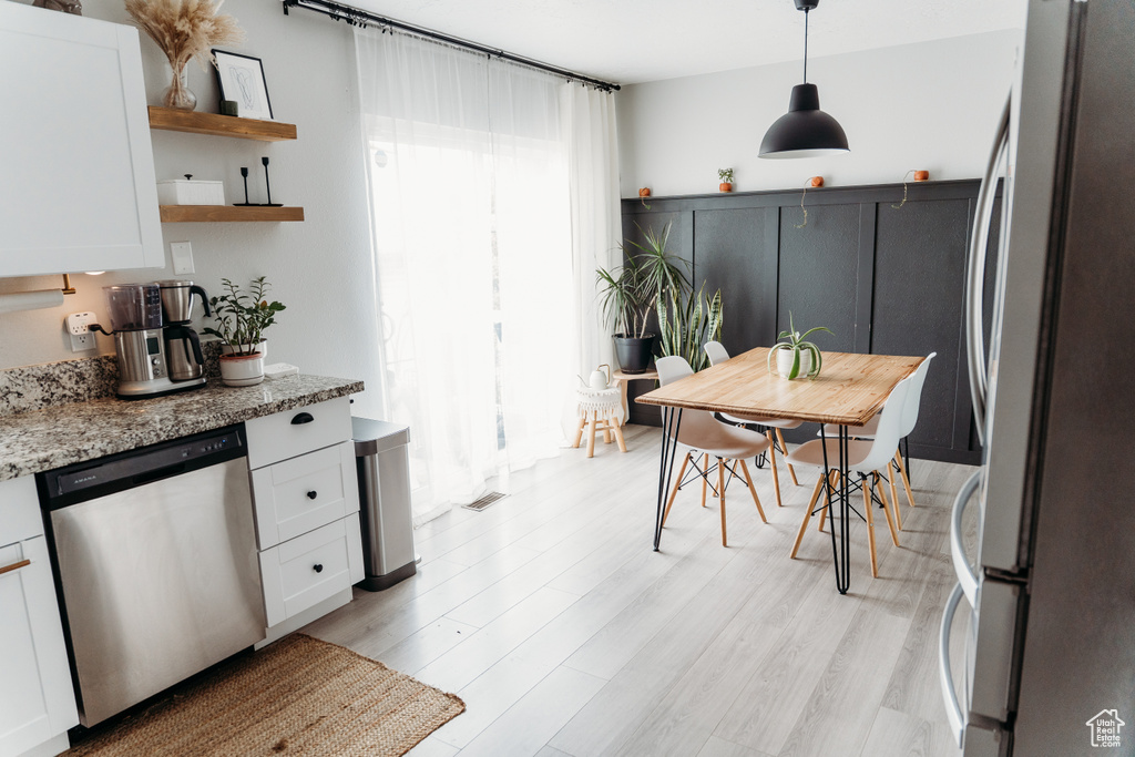 Kitchen featuring appliances with stainless steel finishes, white cabinetry, light wood-style flooring, open shelves, and light stone counters