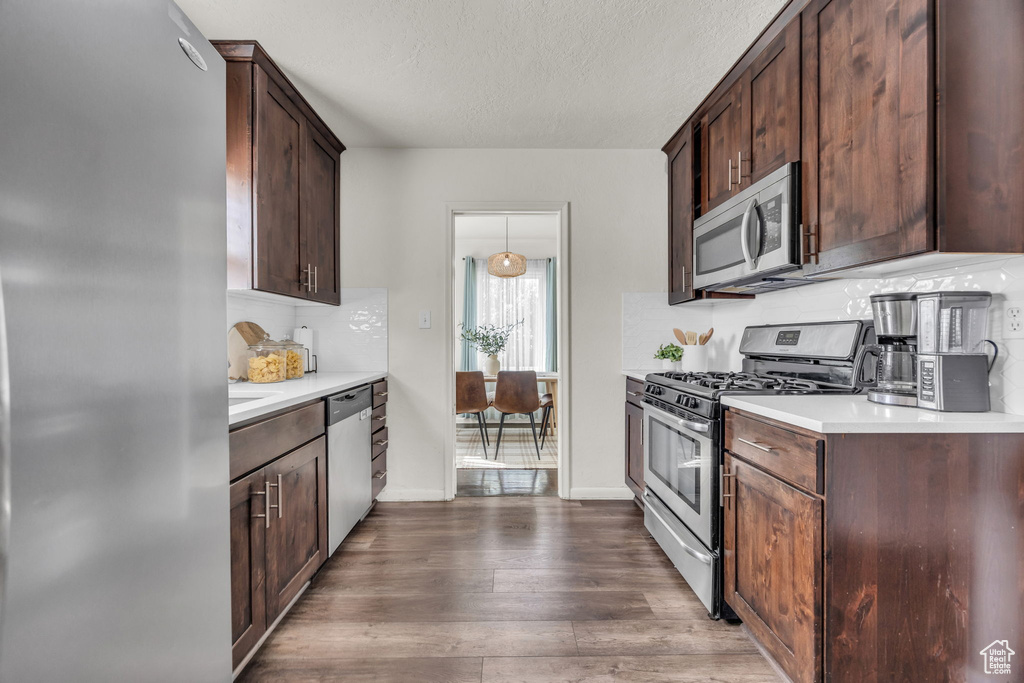 Kitchen featuring appliances with stainless steel finishes, light countertops, dark wood-type flooring, dark brown cabinets, and a textured ceiling