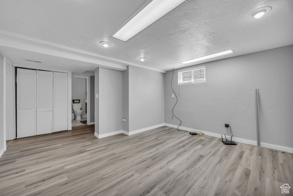 Below grade area featuring baseboards, light wood finished floors, and a textured ceiling