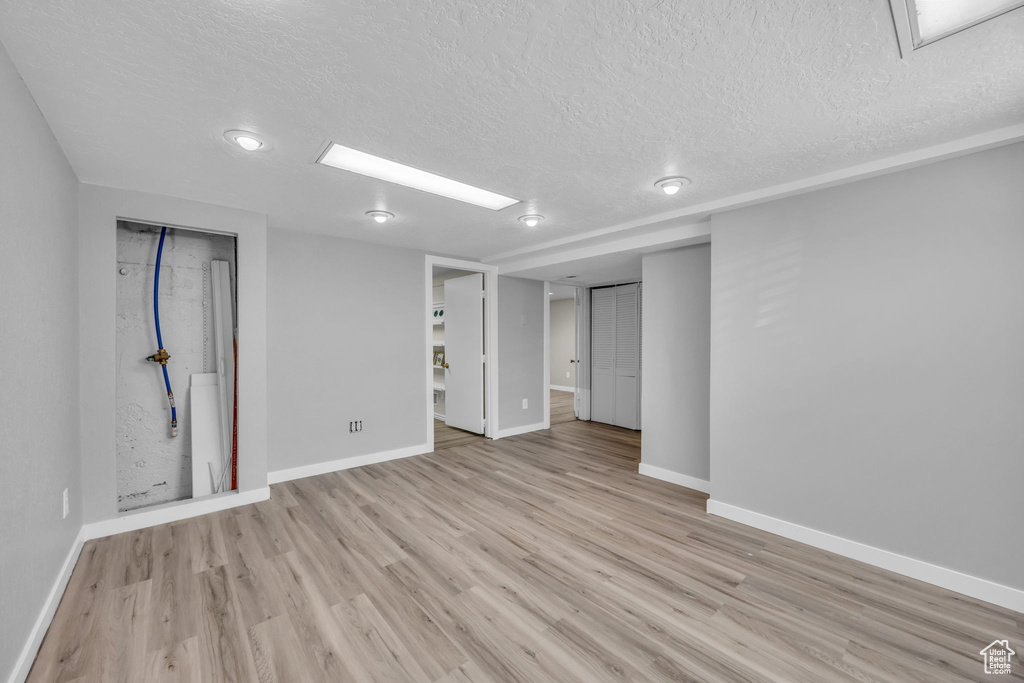 Below grade area with a textured ceiling, baseboards, and light wood-type flooring