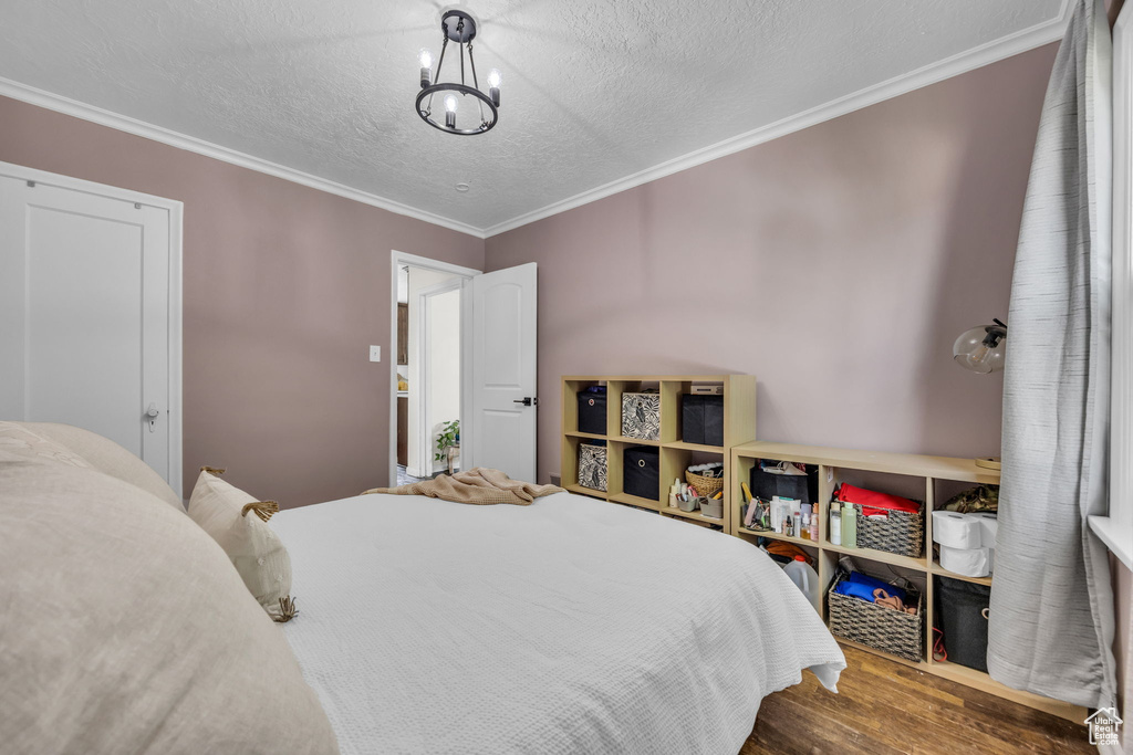 Bedroom with wood finished floors, crown molding, a textured ceiling, and a chandelier