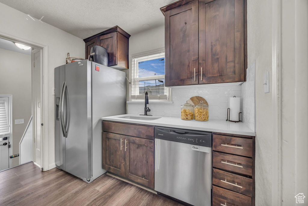 Kitchen with appliances with stainless steel finishes, a sink, wood finished floors, backsplash, and light countertops