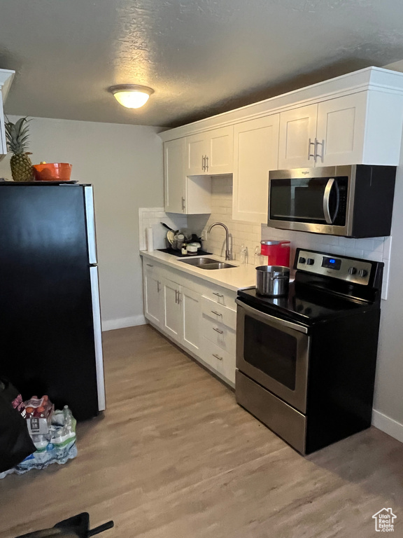 Kitchen featuring appliances with stainless steel finishes, a sink, backsplash, baseboards, and white cabinetry