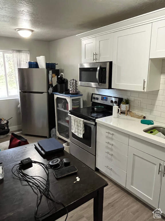 Kitchen featuring appliances with stainless steel finishes, white cabinetry, backsplash, light countertops, and light wood-style floors