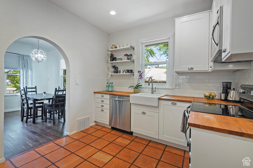 Kitchen featuring wooden counters, appliances with stainless steel finishes, arched walkways, a sink, and backsplash