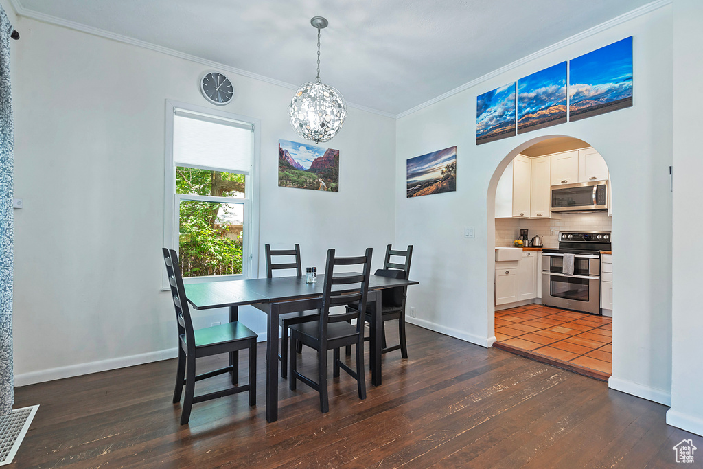 Dining room featuring arched walkways, ornamental molding, dark wood-style floors, a chandelier, and baseboards