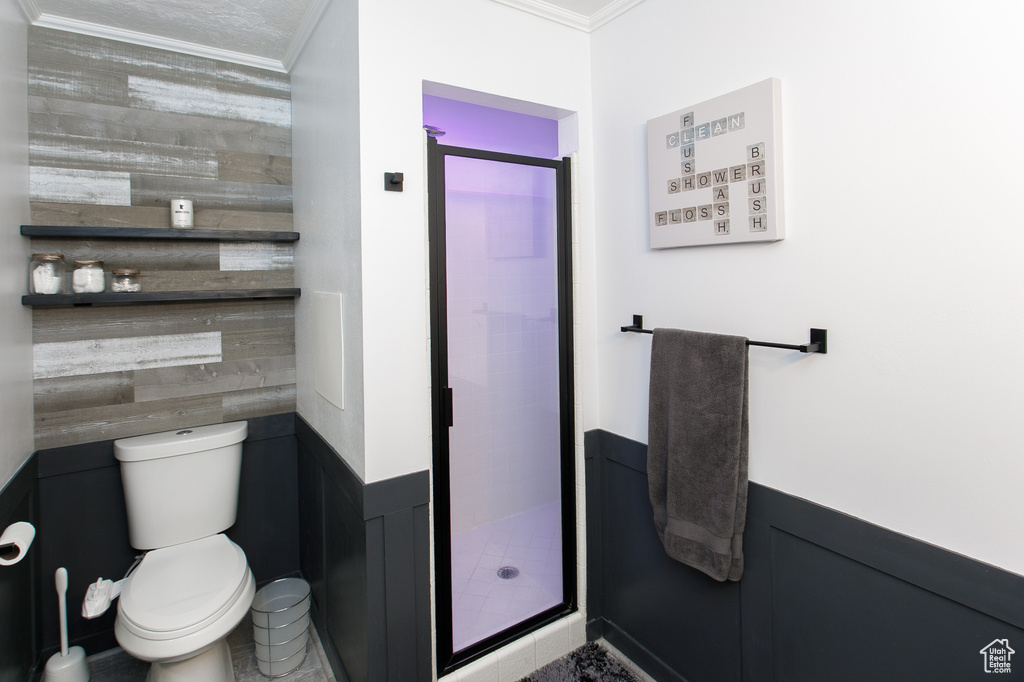 Full bathroom featuring crown molding, a shower stall, toilet, wooden walls, and wainscoting