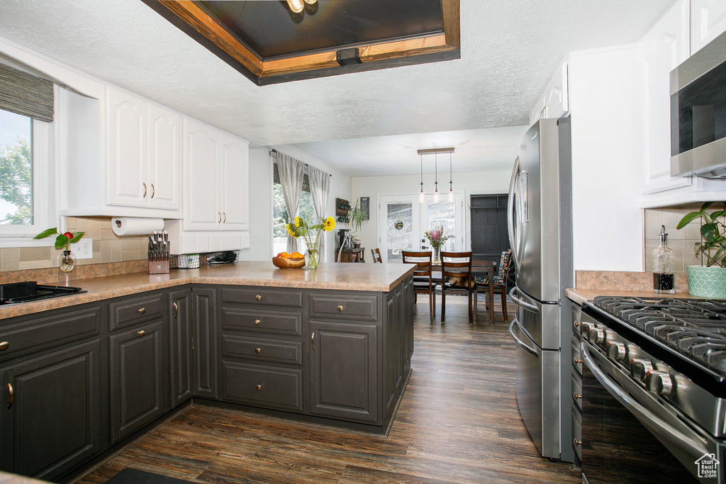Kitchen with stainless steel appliances, white cabinets, a peninsula, tasteful backsplash, and dark wood-style flooring