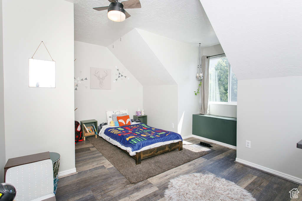 Bedroom featuring wood finished floors, a textured ceiling, vaulted ceiling, baseboards, and ceiling fan