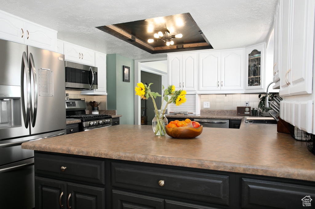 Kitchen with appliances with stainless steel finishes, dark cabinetry, a textured ceiling, dark countertops, and white cabinetry