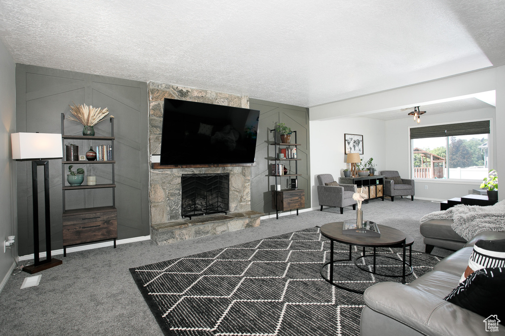 Carpeted living area with baseboards, a stone fireplace, and a textured ceiling
