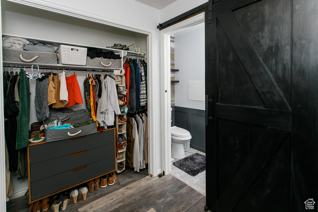 Bathroom with wood finished floors, toilet, a walk in closet, and a wainscoted wall
