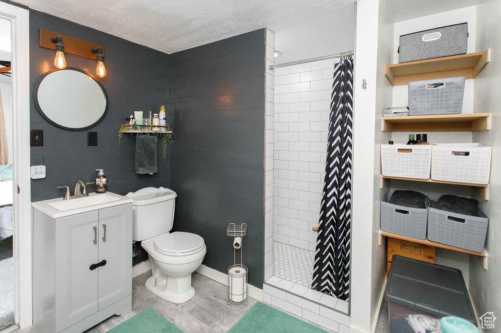 Full bathroom featuring tiled shower, vanity, toilet, a textured ceiling, and baseboards