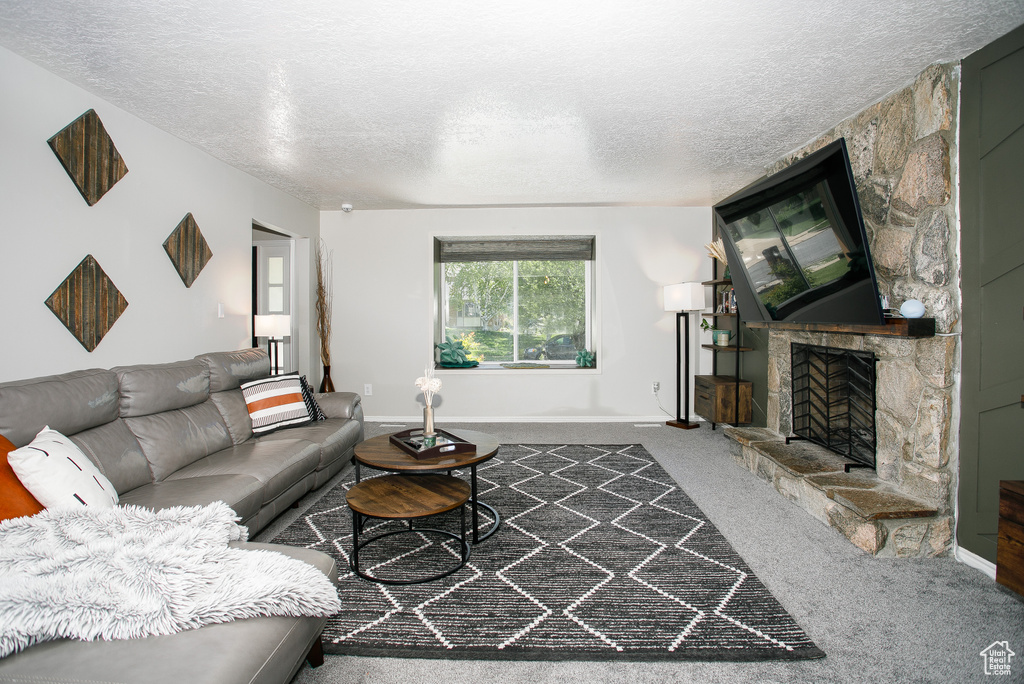 Living room featuring a textured ceiling, a fireplace, carpet floors, and baseboards
