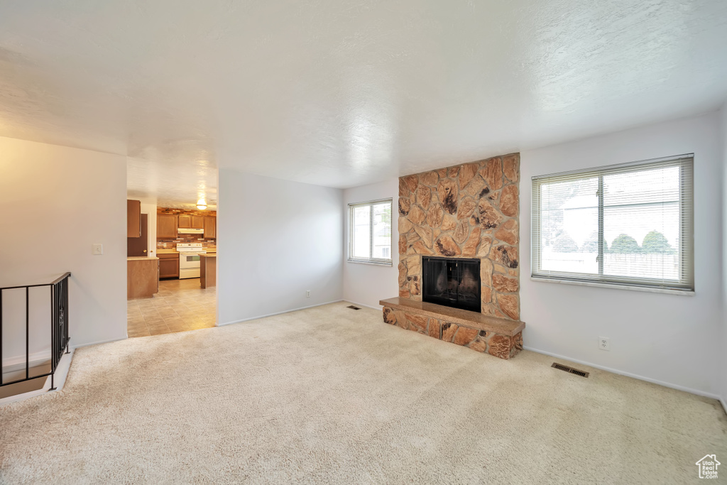 Unfurnished living room featuring light colored carpet, a stone fireplace, and baseboards