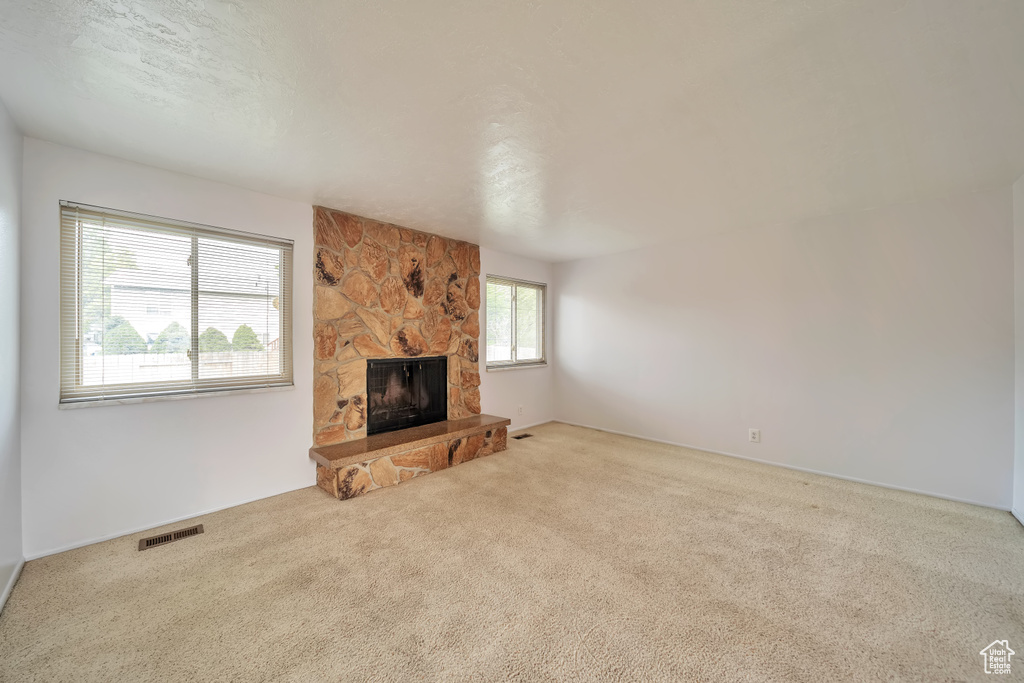 Unfurnished living room featuring carpet floors and a stone fireplace