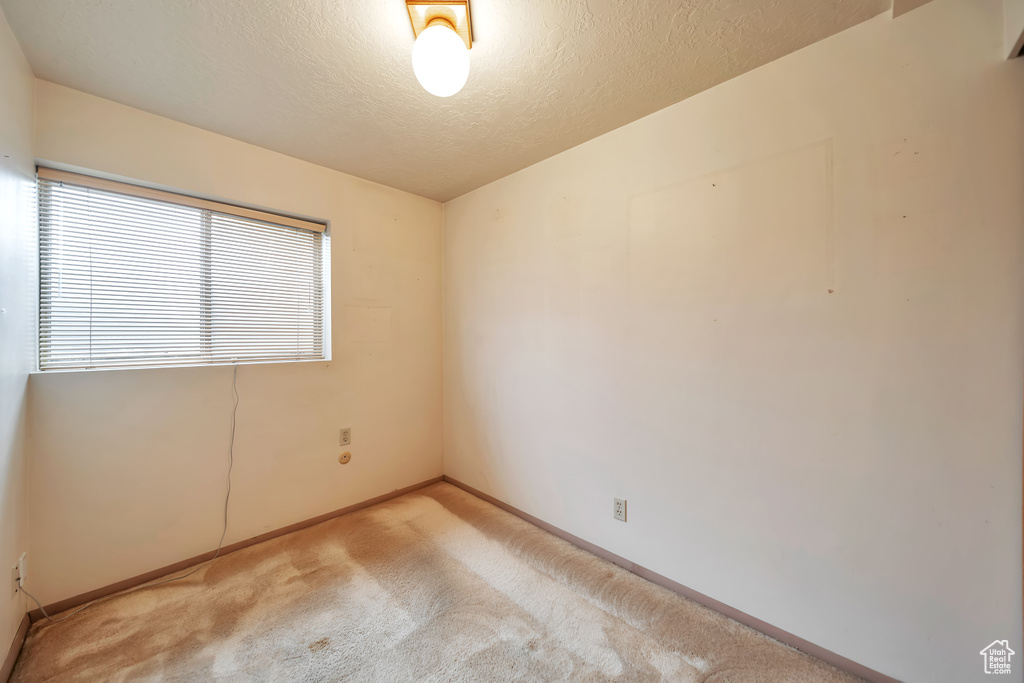 Empty room with carpet flooring, baseboards, and a textured ceiling