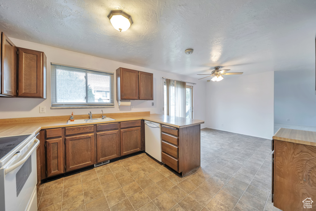 Kitchen with white appliances, a sink, a peninsula, brown cabinetry, and a ceiling fan