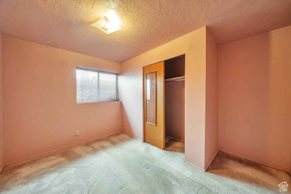 Unfurnished bedroom with carpet, a textured ceiling, a closet, and baseboards