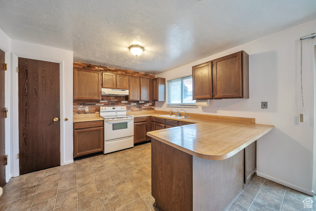 Kitchen with electric range, under cabinet range hood, a peninsula, and light countertops