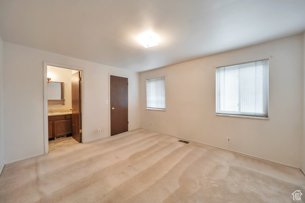 Unfurnished bedroom with light colored carpet, ensuite bathroom, and a sink