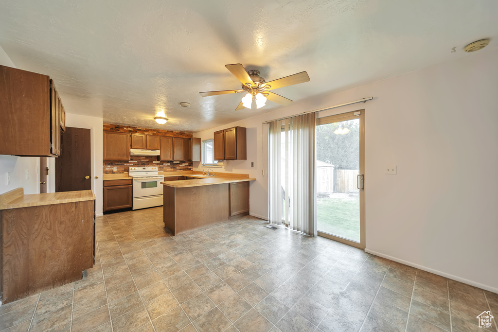 Kitchen with electric range, a peninsula, under cabinet range hood, brown cabinets, and a sink