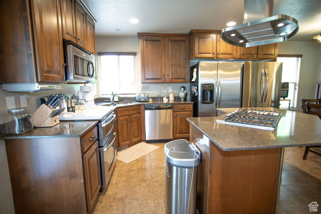 Kitchen featuring stainless steel appliances, island range hood, a sink, light tile patterned floors, and a center island
