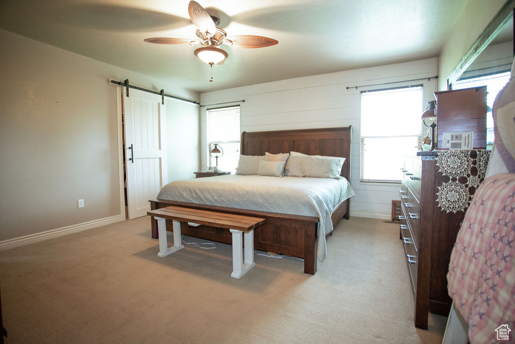 Bedroom with a barn door, light carpet, ceiling fan, and baseboards