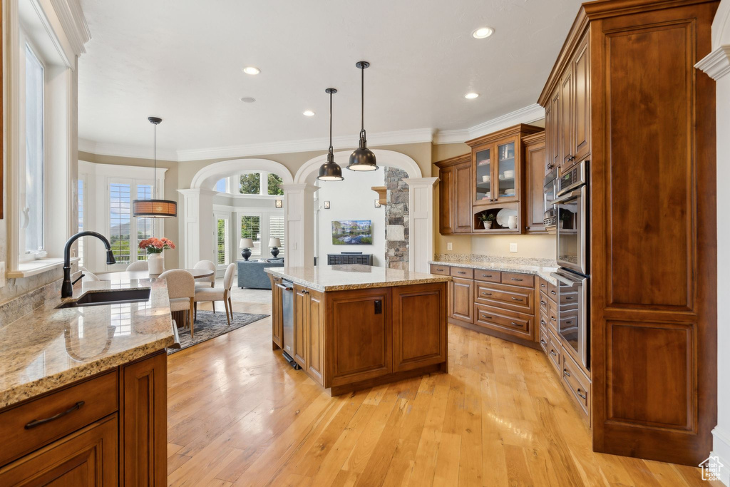 Kitchen featuring a sink, decorative columns, brown cabinets, light wood-type flooring, and glass insert cabinets