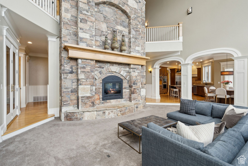 Living room featuring decorative columns, carpet, a high ceiling, a stone fireplace, and ornamental molding