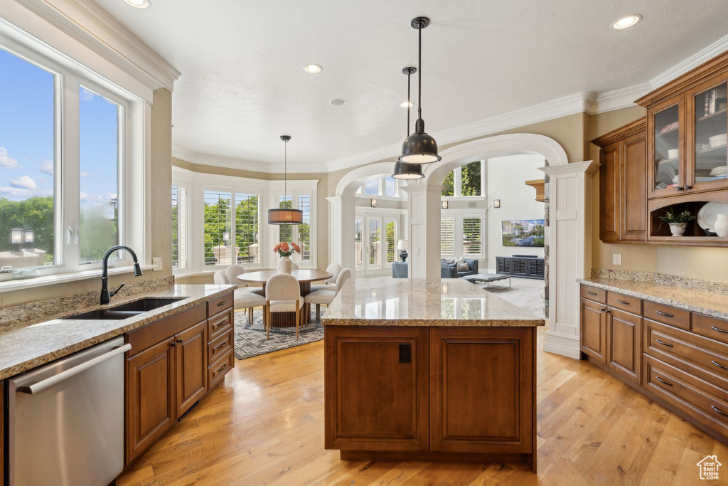 Kitchen featuring stainless steel dishwasher, decorative columns, a sink, arched walkways, and brown cabinetry