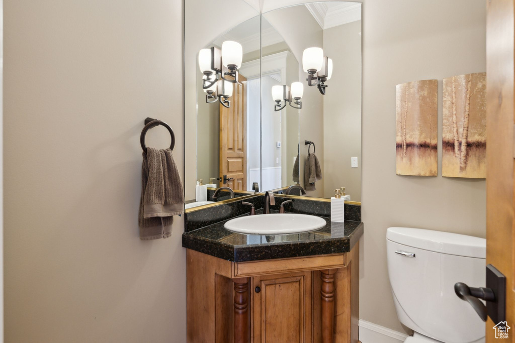 Half bath featuring vanity, toilet, and crown molding