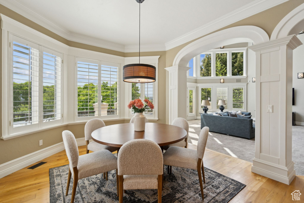 Dining space featuring decorative columns, healthy amount of natural light, crown molding, and light wood finished floors