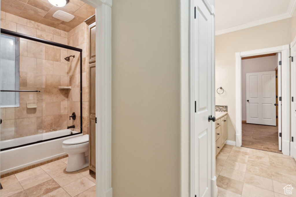Bathroom featuring toilet, vanity, shower / bath combination with glass door, ornamental molding, and tile patterned floors