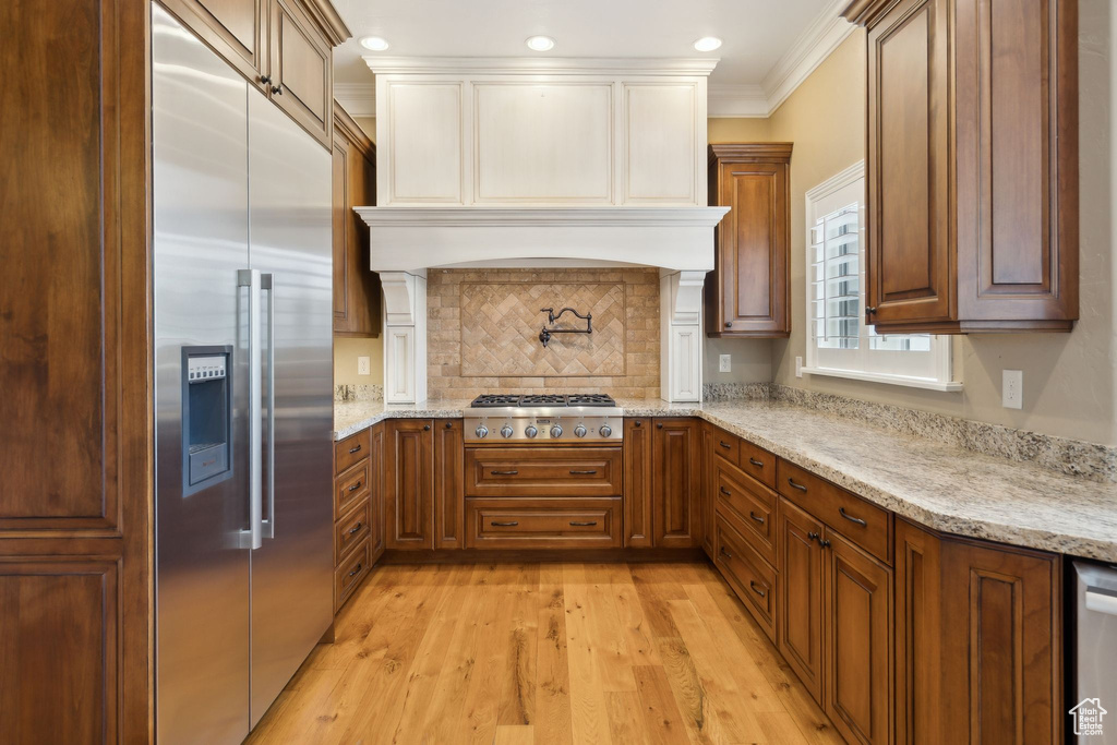 Kitchen featuring stainless steel appliances, light wood-style floors, tasteful backsplash, crown molding, and light stone counters