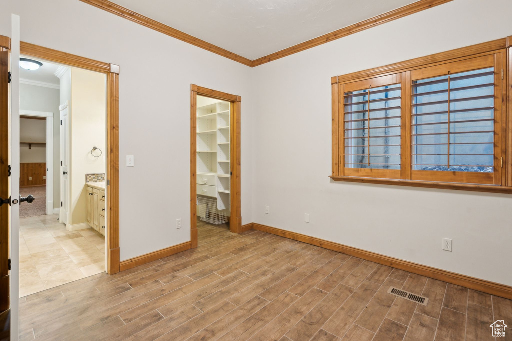 Unfurnished bedroom with crown molding, baseboards, wood finished floors, a walk in closet, and a closet