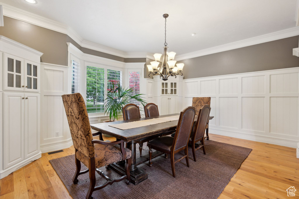 Dining room with a decorative wall, a chandelier, light wood-type flooring, crown molding, and a wainscoted wall